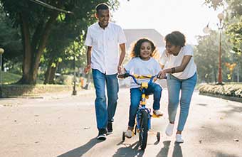 mom and dad teaching young daughter how to ride a bike