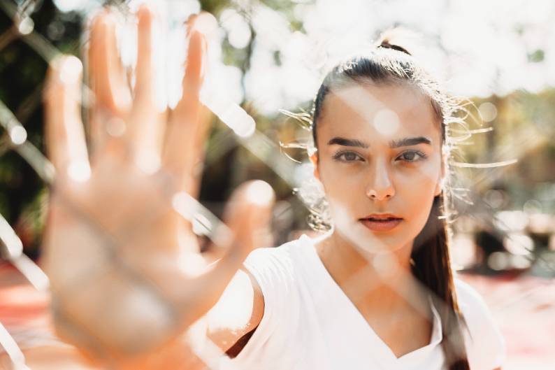 Young women holding her hand against a chain link fence